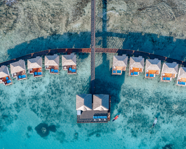 Aerial shot of overwater bungalows on a calm, turquoise sea at dusk.