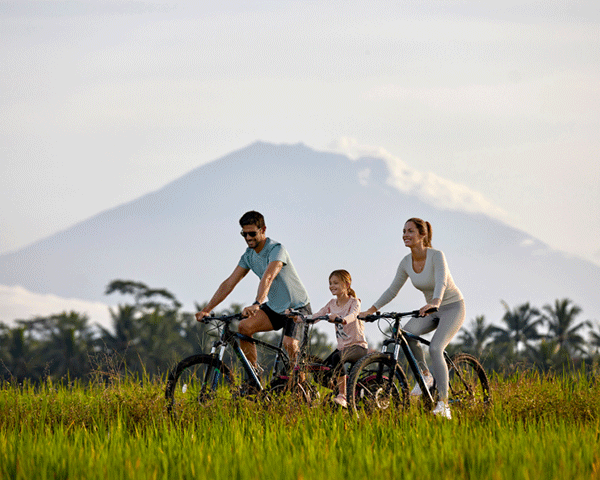 A family of three bicycles through a grassy area with mountains in the distance.