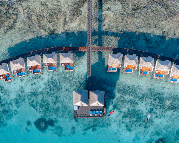 Aerial shot of overwater bungalows on a calm, turquoise sea at dusk.