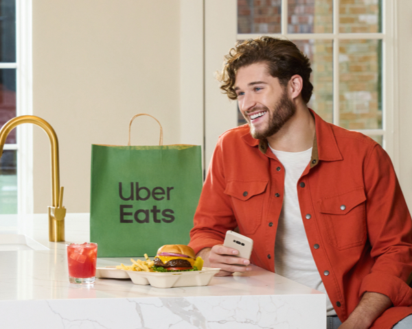 Man holding phone sits at kitchen island about to enjoy an Uber Eats order.