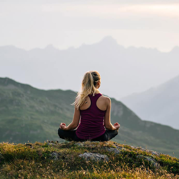 A young woman meditating outdoors in front of a mountain vista