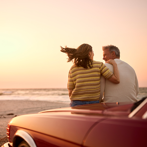 A couple sitting on the hood of a car next to the ocean