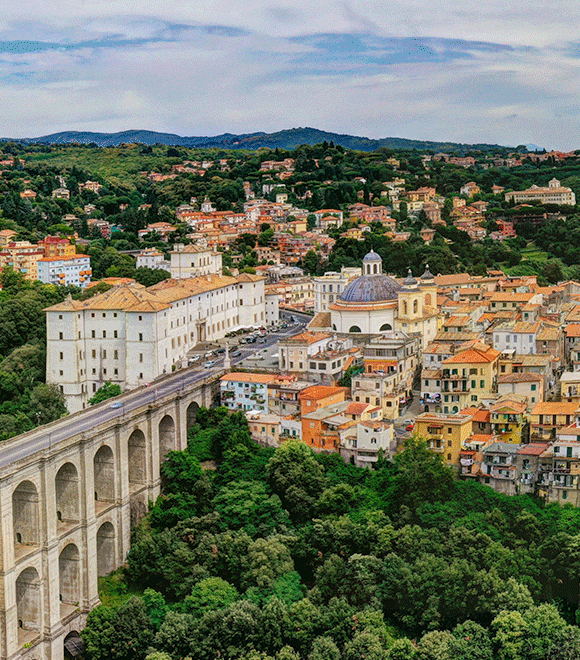 Scenic view of Ariccia, Italy, featuring a bridge spanning a river amidst historic buildings and lush greenery
