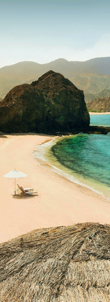 Two beach chairs under an umbrella on a beach.