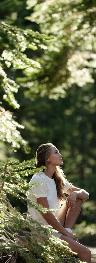Woman sitting on a cliff under trees on an outdoor hike.