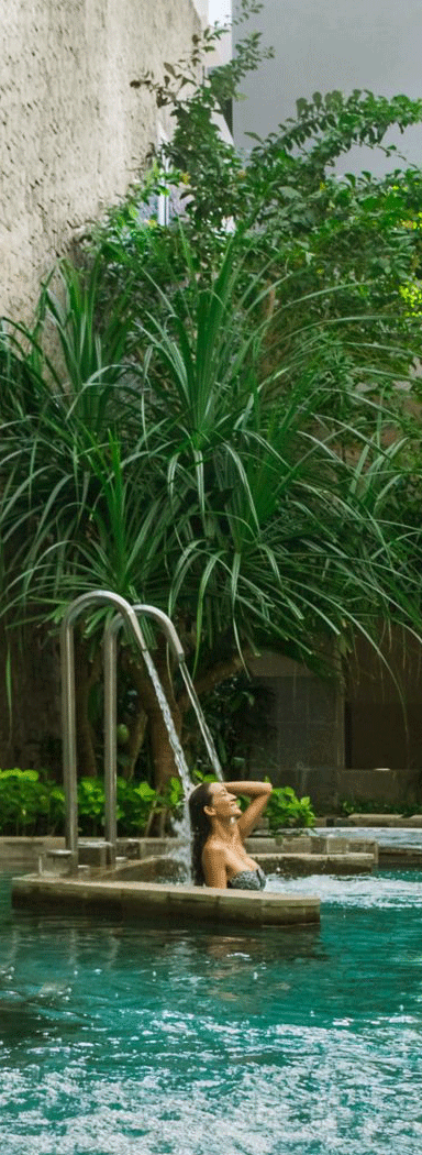 Woman in an outdoor pool surrounded by lush greenery.