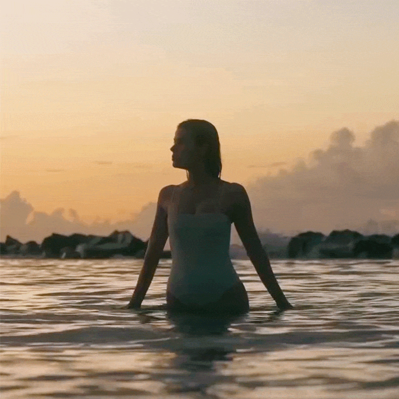 Woman walks through the sea at sunset.