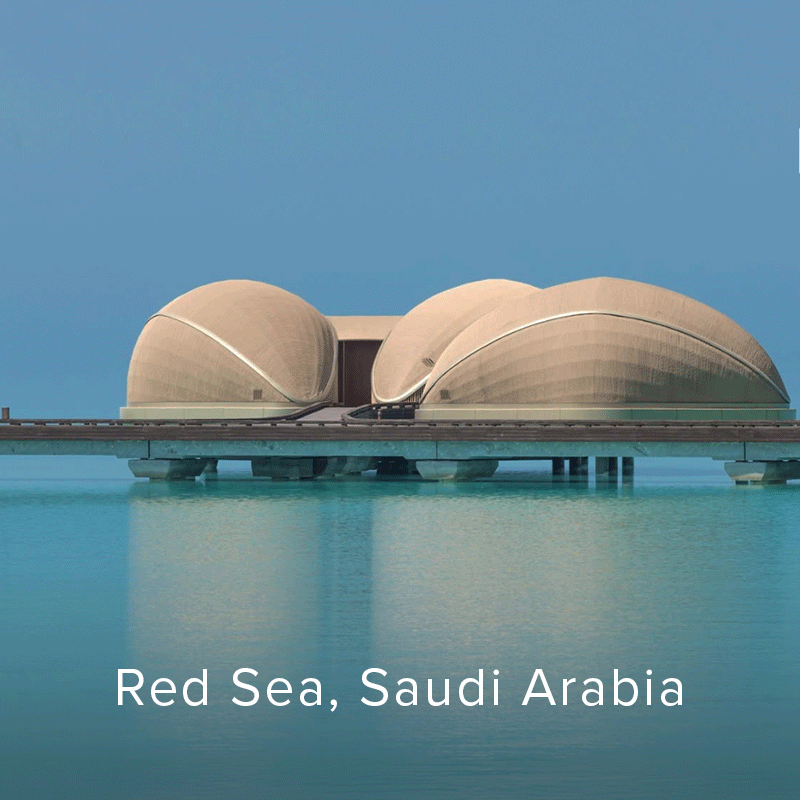 Hotel villas span a calm turquoise waterfront beneath a clear blue sky.