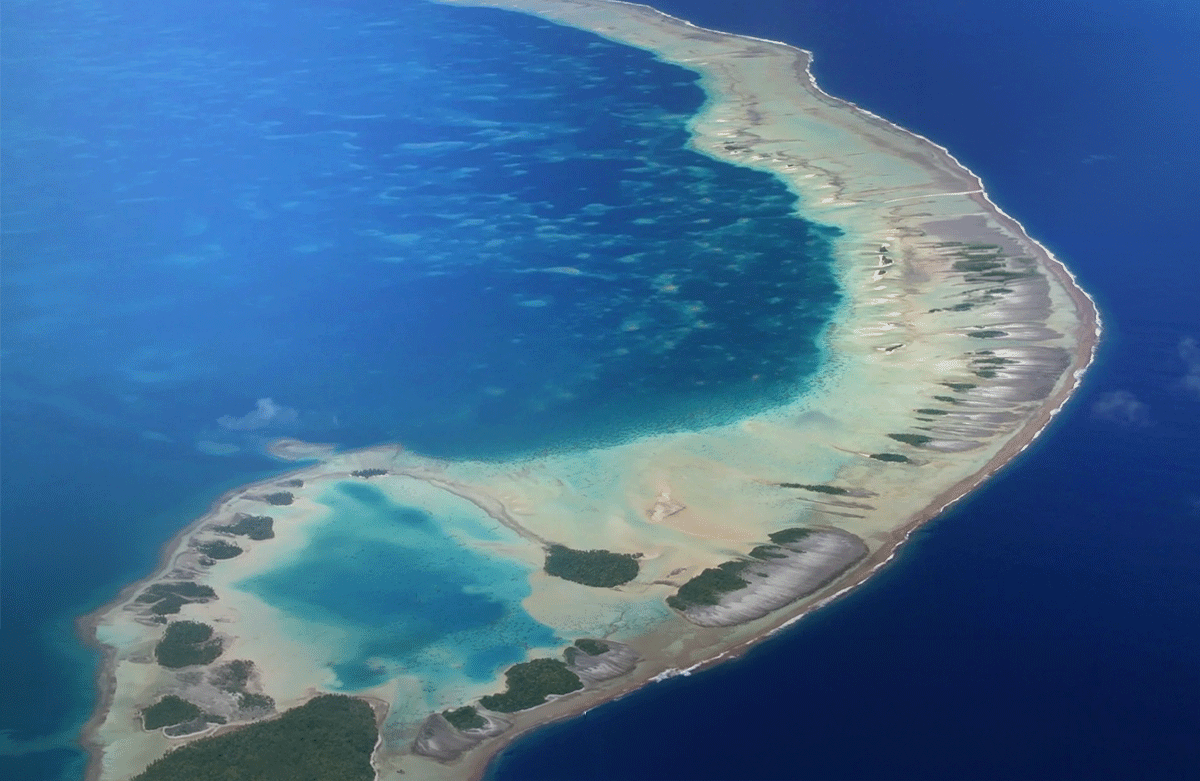 Ein geschwungenes Korallenatoll, umgeben vom tiefblauen Ozean.